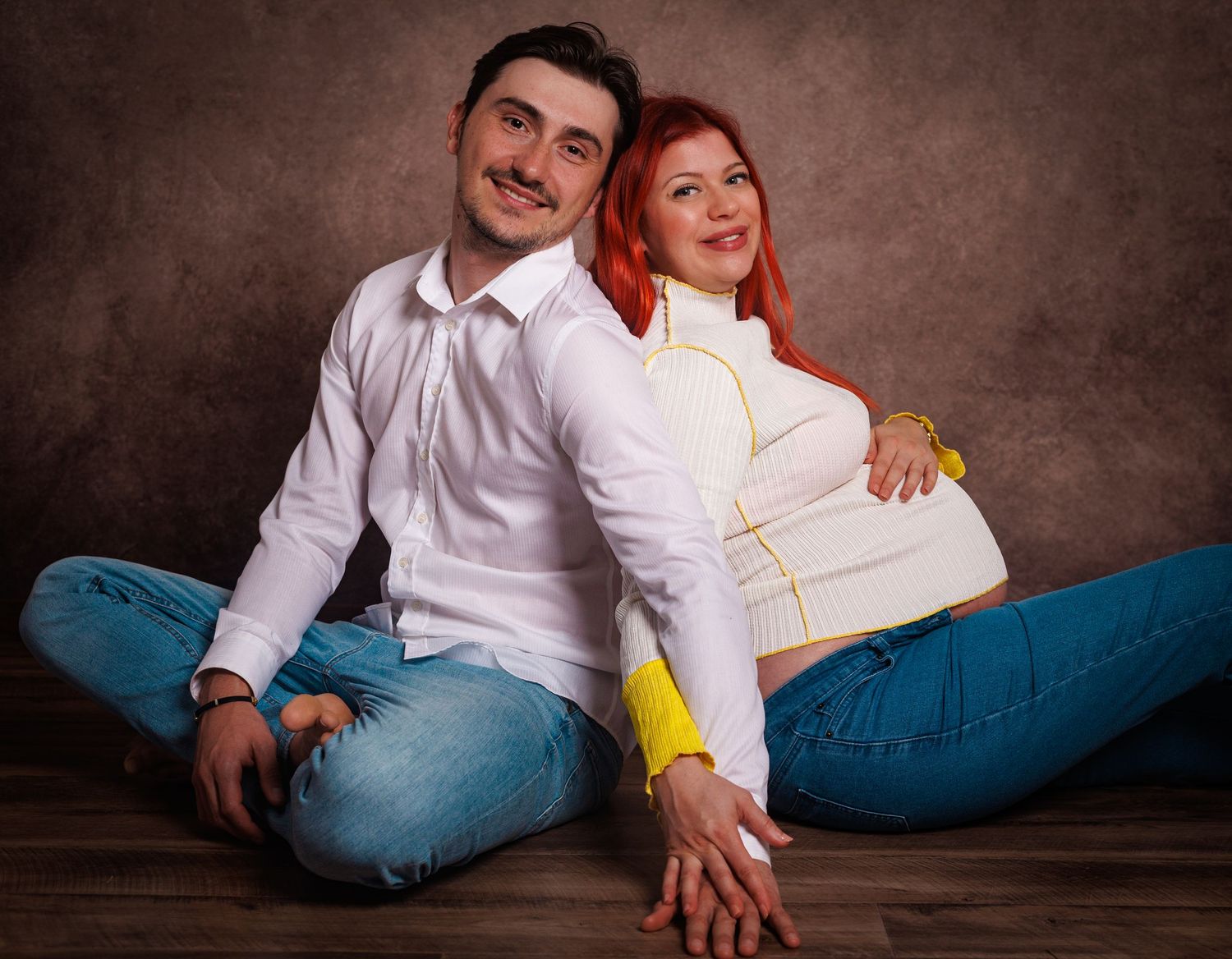 Seated studio portrait of an expectant couple smiling together