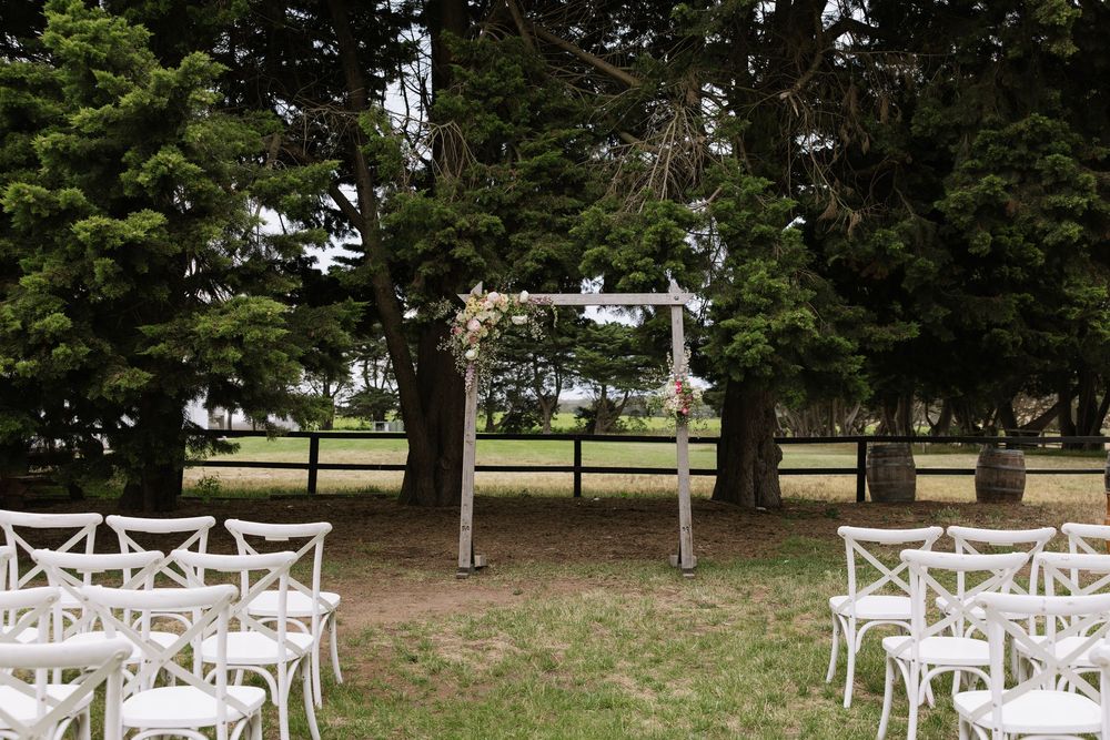 Outdoor wedding ceremony setup with white chairs and a rustic wooden arch surrounded by tall green trees.