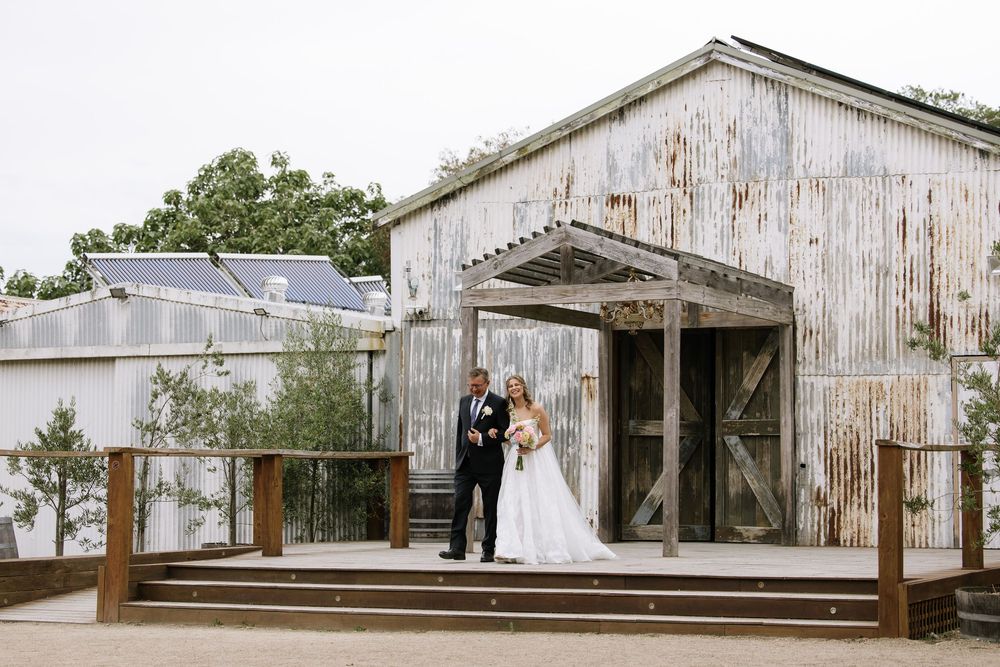 Bride and groom posing in front of a rustic corrugated metal barn venue on their wedding day.
