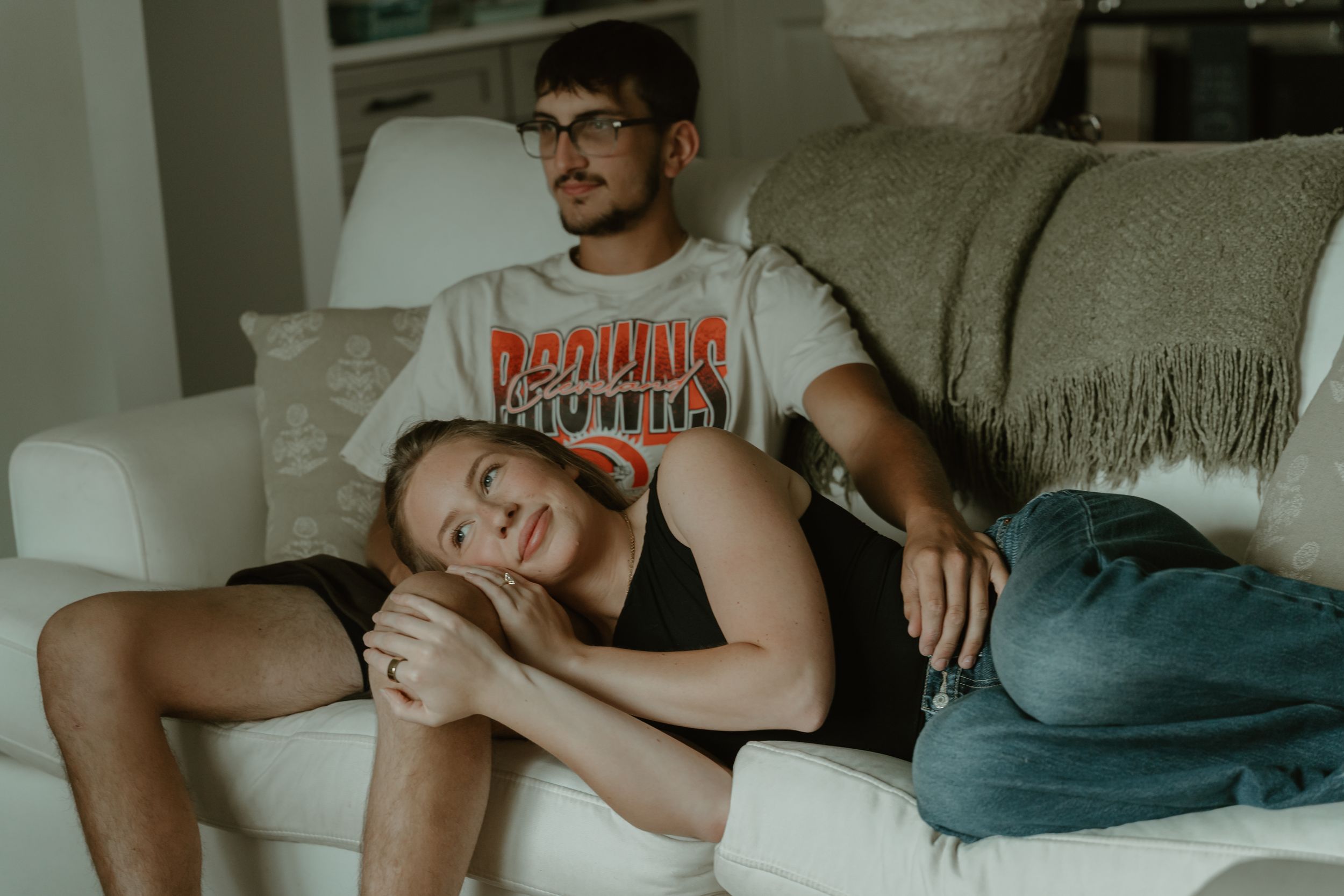 Young couple relaxing on white couch, woman resting head on mans lap in cozy living room setting.