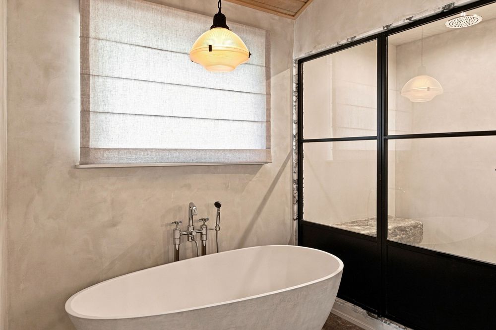 Modern bathroom with freestanding white soaking tub, pendant light, and black-framed glass shower enclosure.