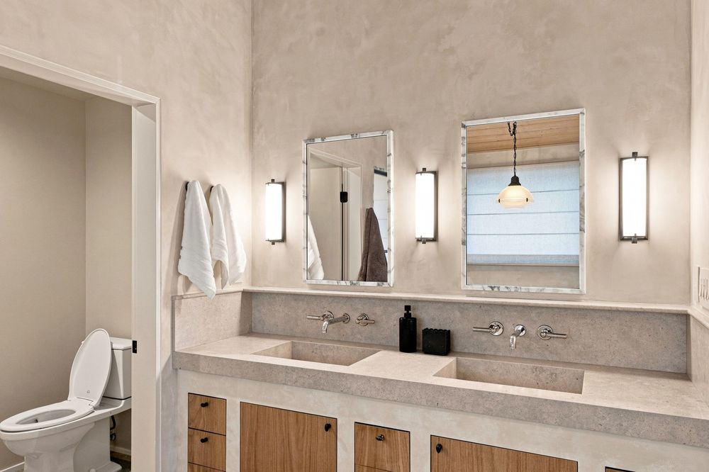 Modern bathroom with double stone sink vanity, wood cabinets, wall sconces, and framed mirrors above.