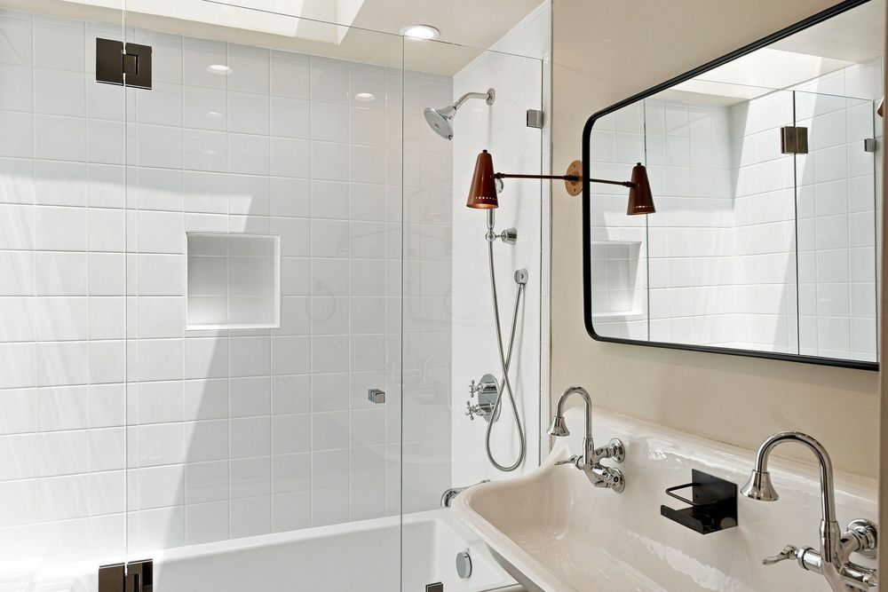 Modern bathroom with glass shower, white subway tiles, chrome fixtures, wall-mounted mirror, and elegant double sink vanity.