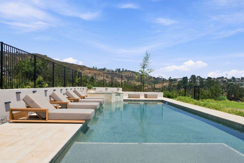 Luxury infinity pool with lounge chairs overlooking lush green hills under a bright blue sky.