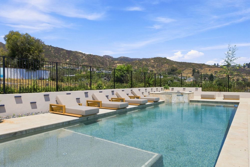 Luxury outdoor pool with lounge chairs and mountain views under a blue sky in a resort-style setting.