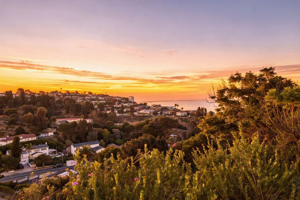 Stunning coastal sunset over a hillside town with vibrant orange and pink skies reflecting over the ocean.