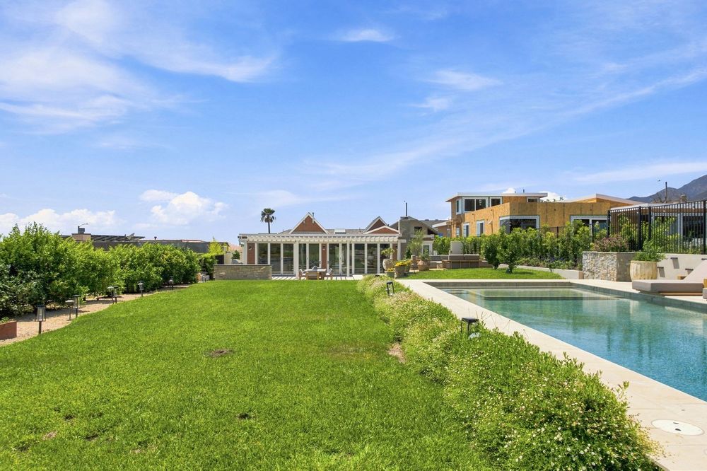 Luxury estate with lush green lawn, pool, and elegant pavilion under a bright blue sky.