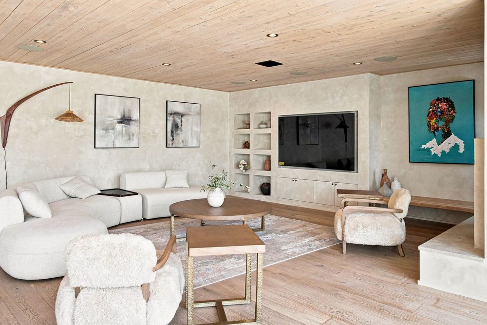 Modern living room with white sofas, wood ceiling, built-in TV shelving, and colorful artwork on textured walls.