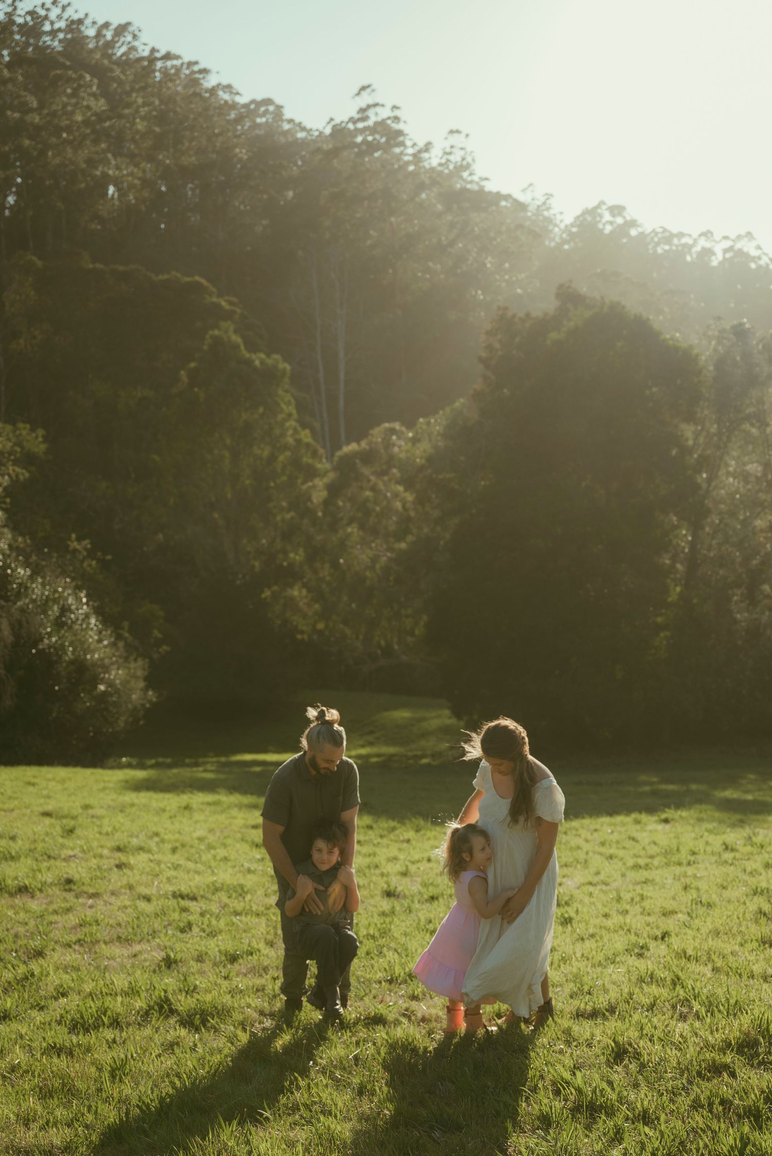 Family of four enjoying a sunny day in a lush green meadow surrounded by tall trees in warm golden light.