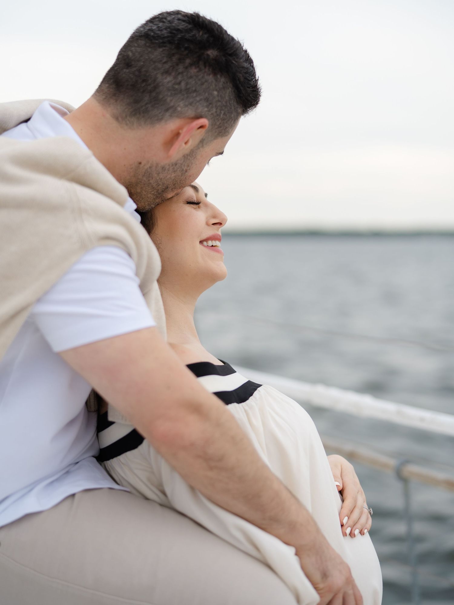 A man wraps his arms around his pregnant wife on a boat in the bay.