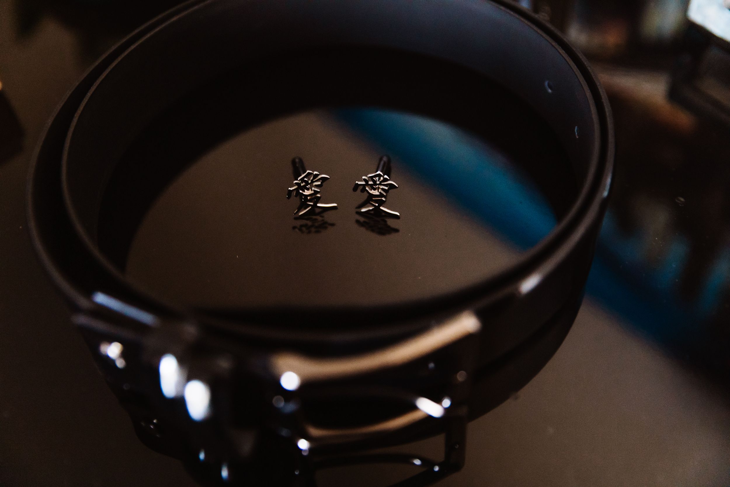 Small silver rose stud earrings displayed on a black leather belt coiled inside a dark drum.