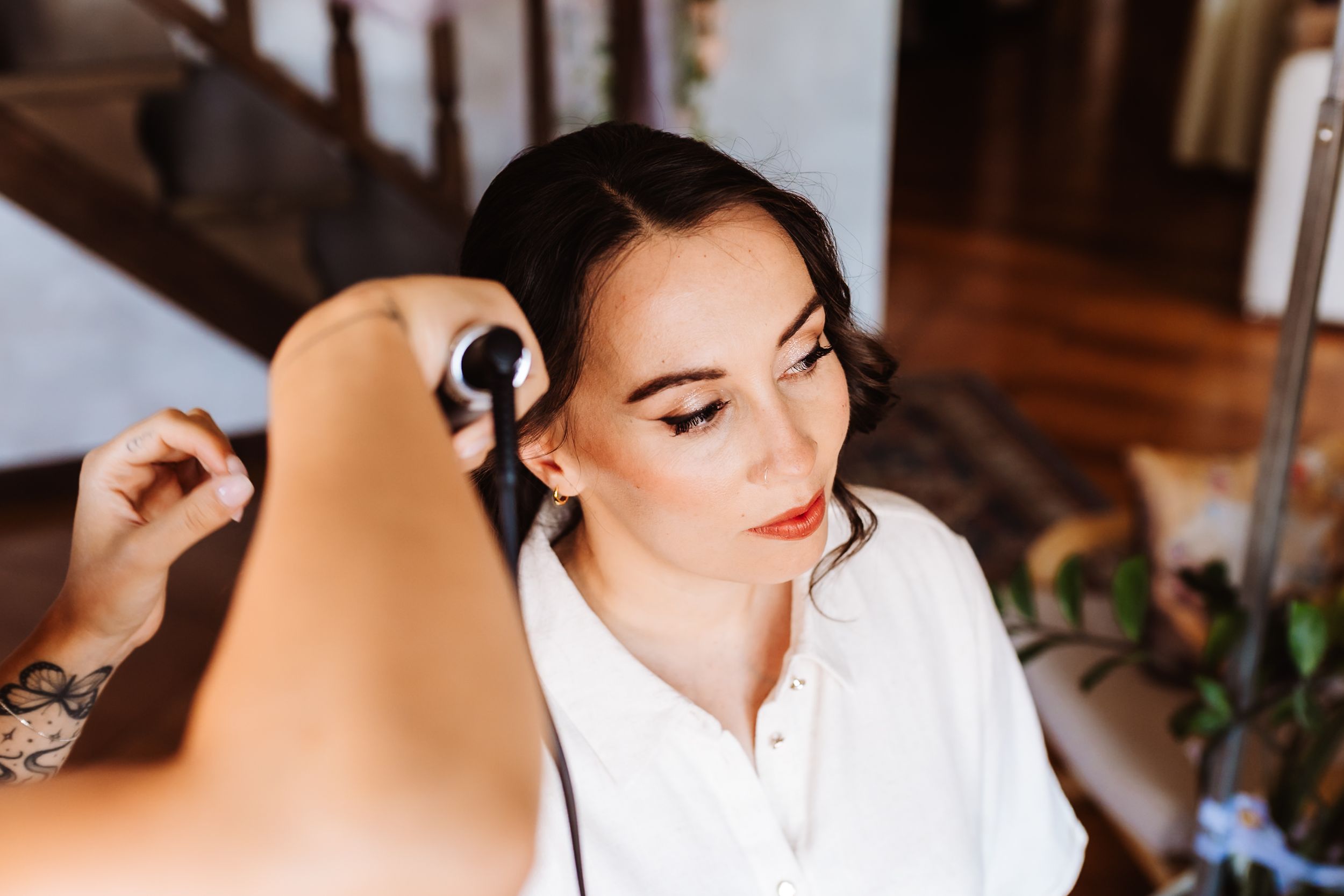 A makeup artist applies finishing touches to a brunette bride in a white robe before her wedding ceremony.