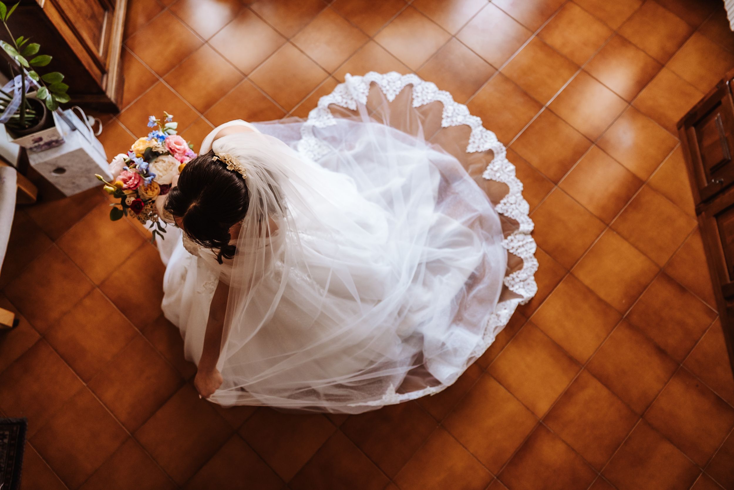 Aerial view of a bride in a white wedding gown with floral crown on terracotta tile floor.