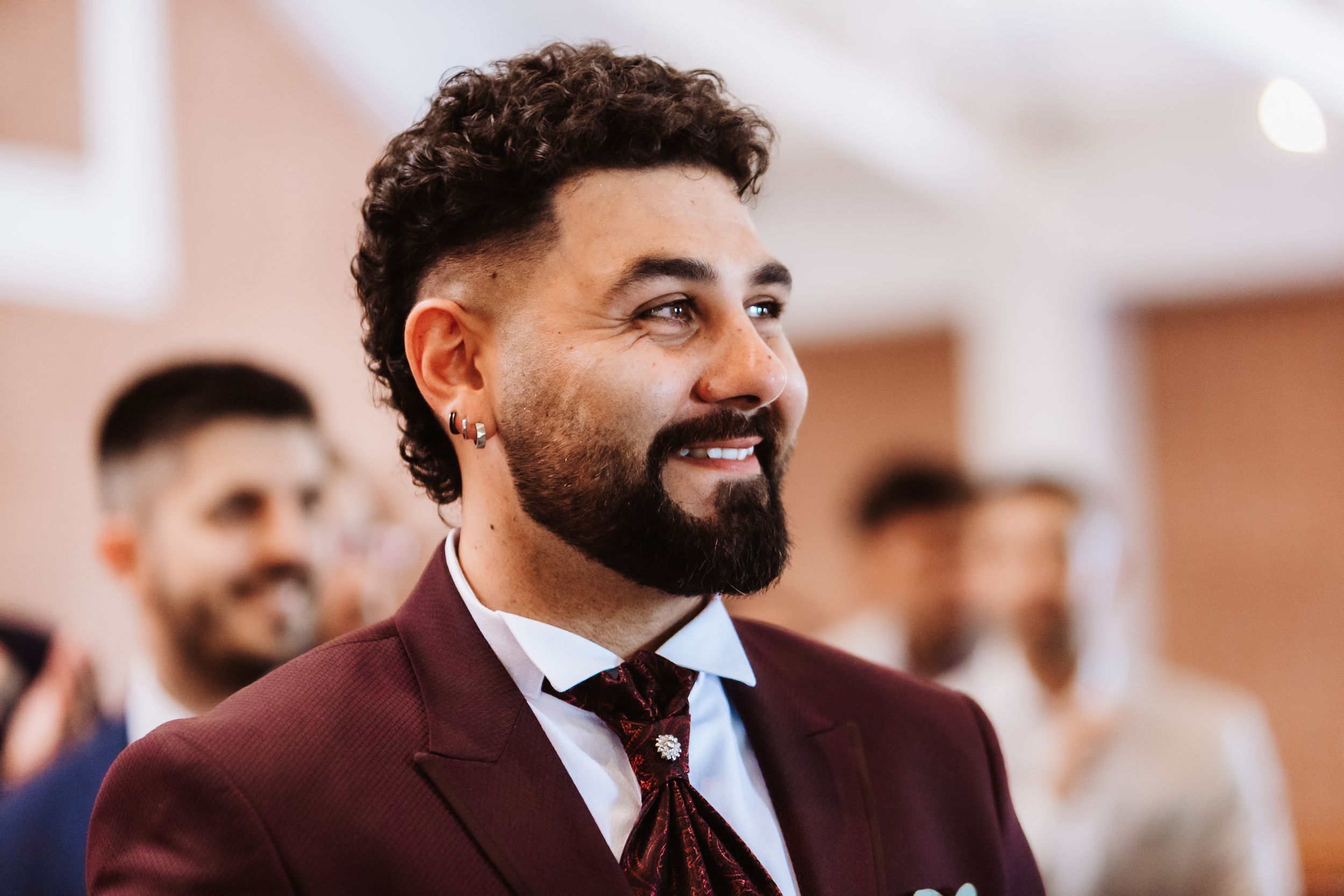 Smiling bearded man in a burgundy suit with a white shirt and dark tie at a formal event.
