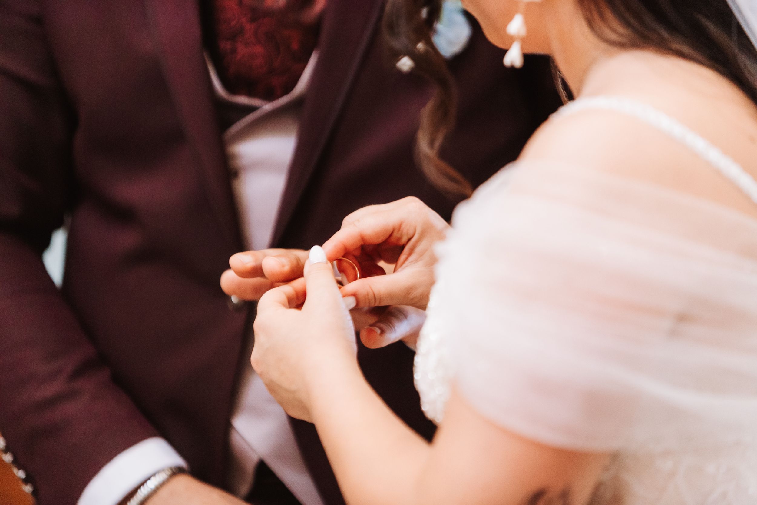 Bride placing a wedding ring on groom's finger during a ceremony, close-up of hands exchanging rings.