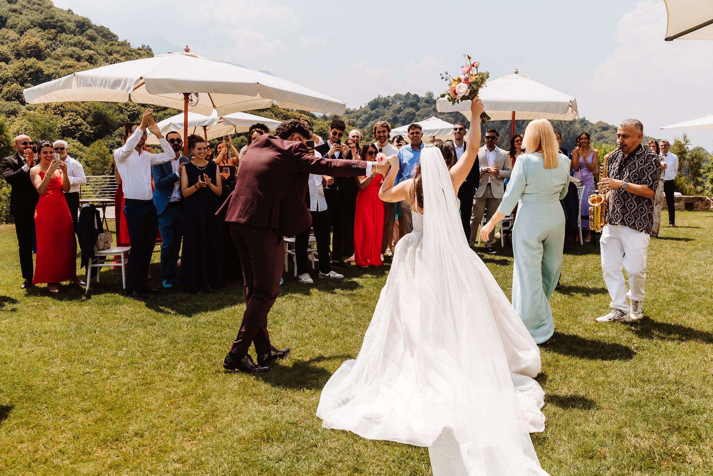 Bride and groom celebrate with guests on sunny lawn at outdoor wedding reception.