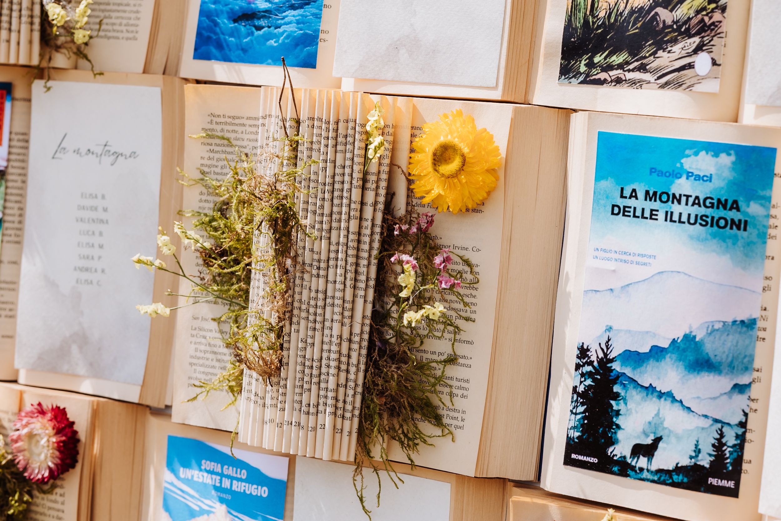 Artistic display of books, dried flowers, and Italian mountain-themed postcards arranged on a wooden board.