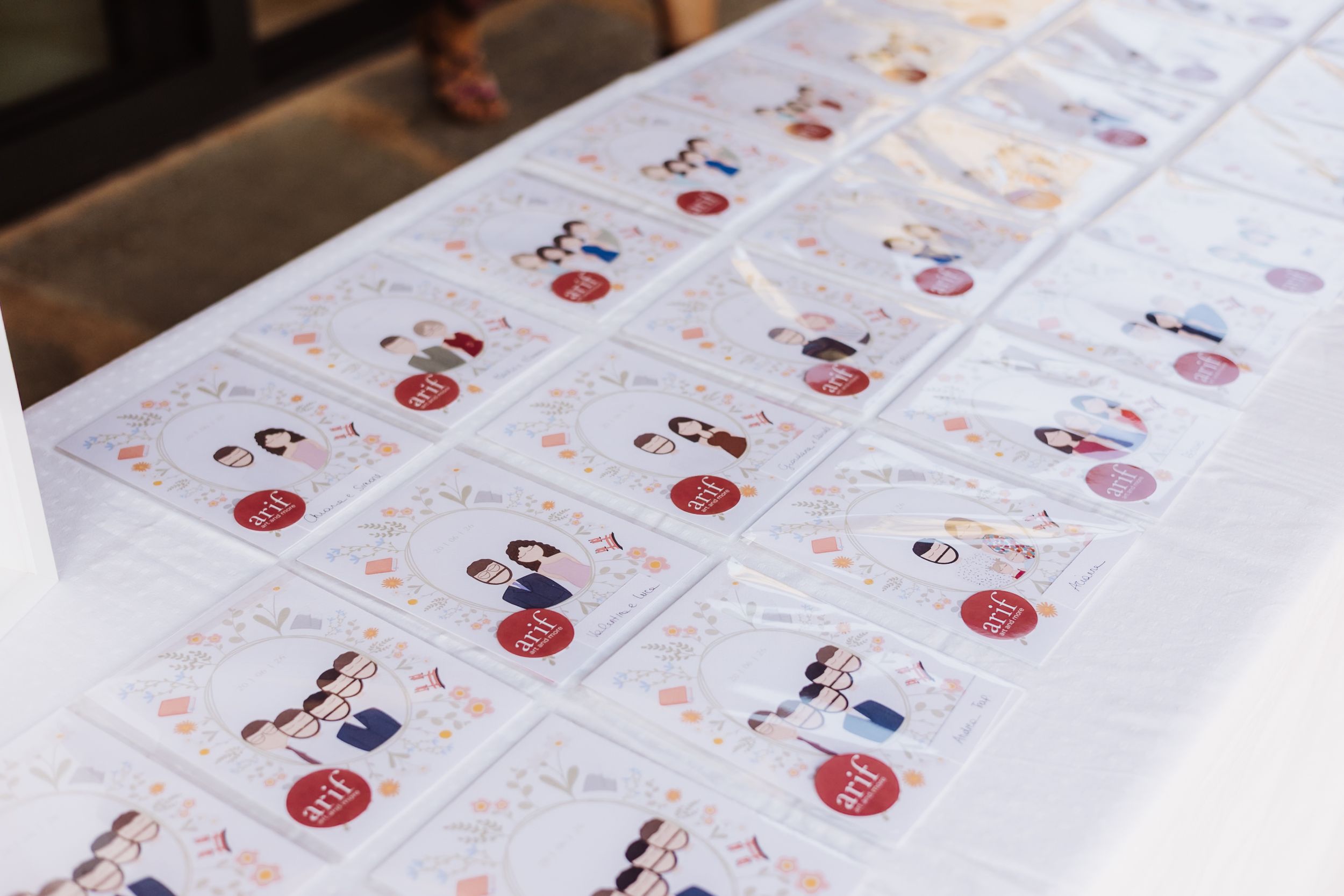 Close-up of illustrated wedding seating cards arranged in rows on a white table at an outdoor event.