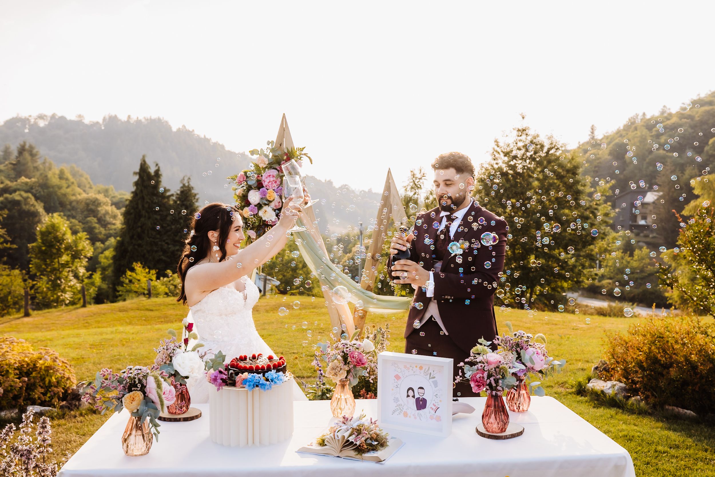 Bride and groom celebrate outdoors at a floral-decorated wedding table with mountains in the background.