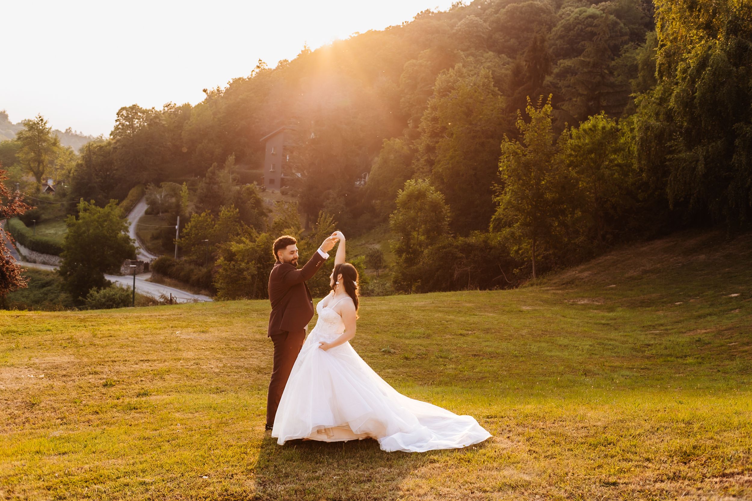 Bride and groom dancing in a sunlit meadow with lush green hills in the background.