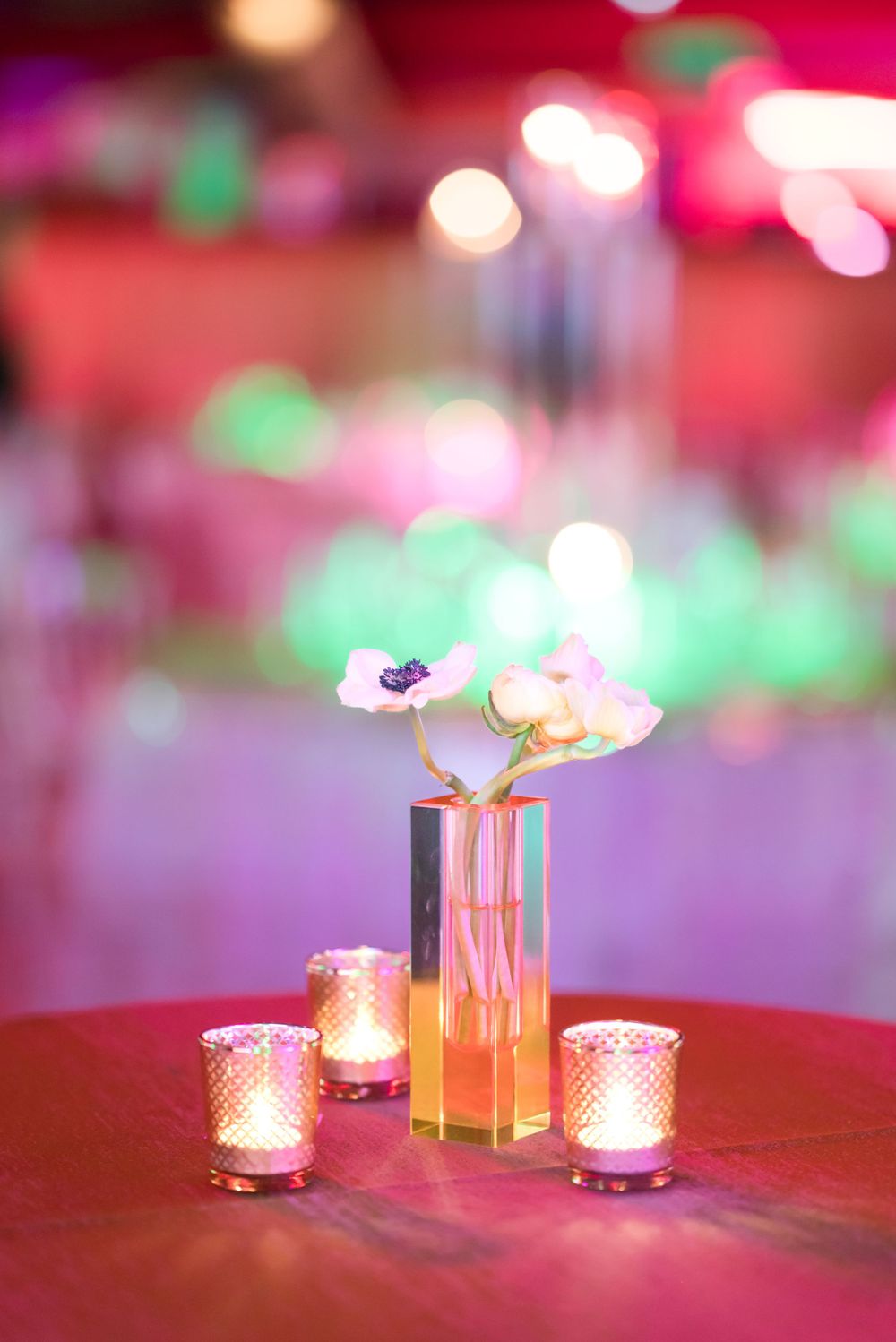 Elegant table centerpiece with delicate flowers in a slim vase and glowing votives creating romantic ambient lighting.
