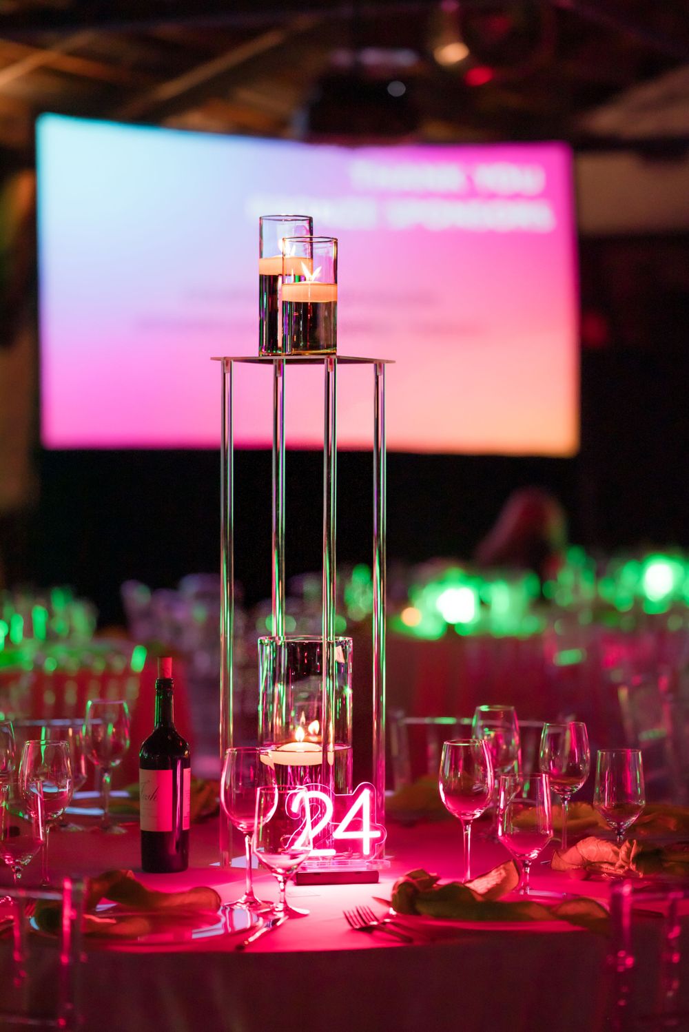 Modern event table setting with illuminated centerpiece and wine glasses in pink lighting.