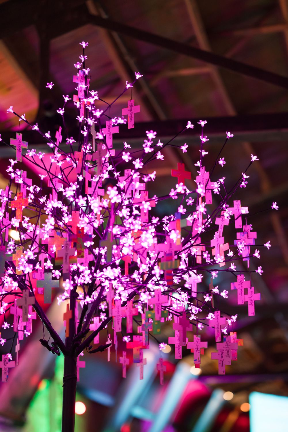 Illuminated pink artificial tree with glowing cross decorations in dark event space.