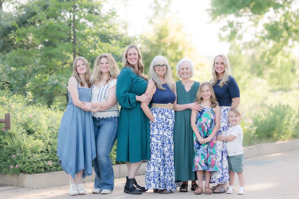 A multi-generational group poses together outdoors wearing flowing dresses in coordinating blue and floral patterns.