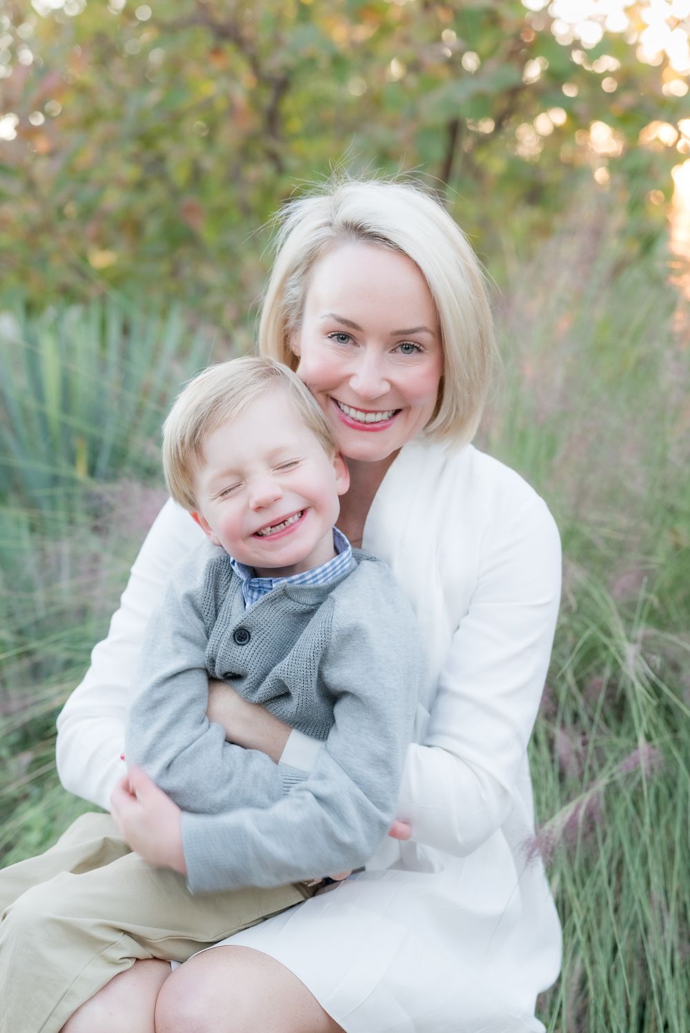 Parent in white sweater hugs child in grey outfit during outdoor portrait session.