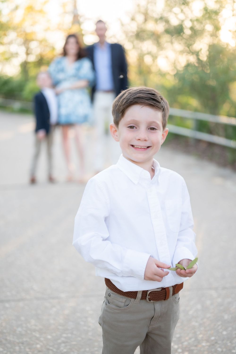 Young boy in crisp white shirt poses outdoors with family visible in background.