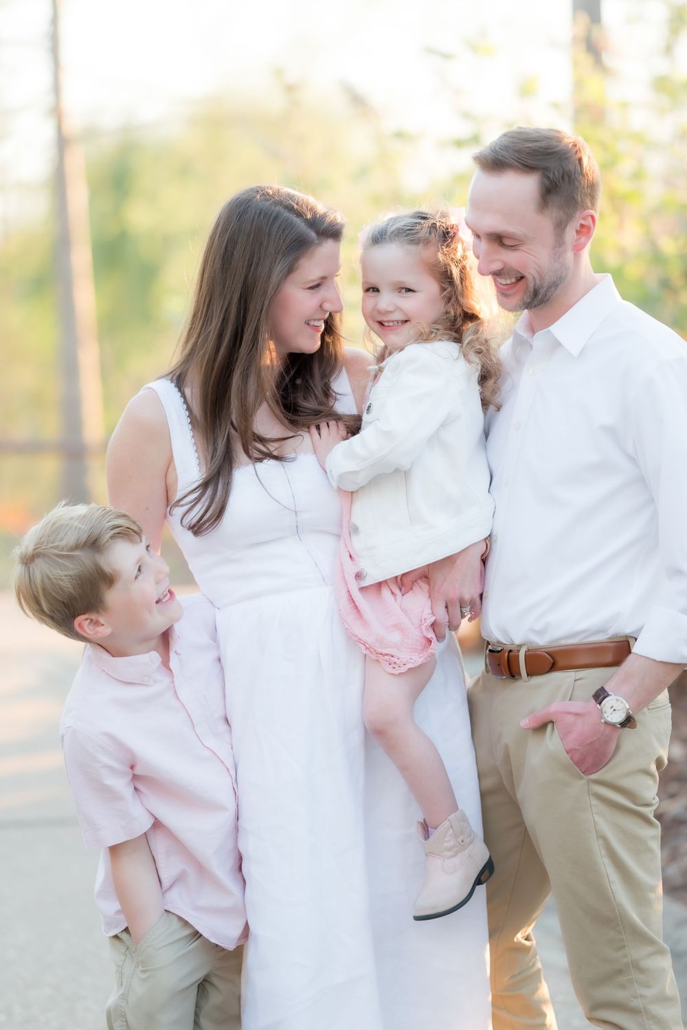 Family photo session outdoors with coordinating pink and white outfits in warm golden light.
