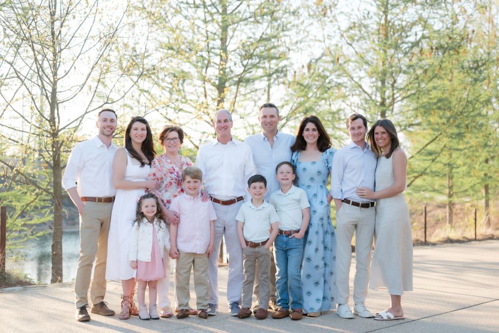 Large extended family gathering posed together outdoors in coordinated pastel and neutral outfits.
