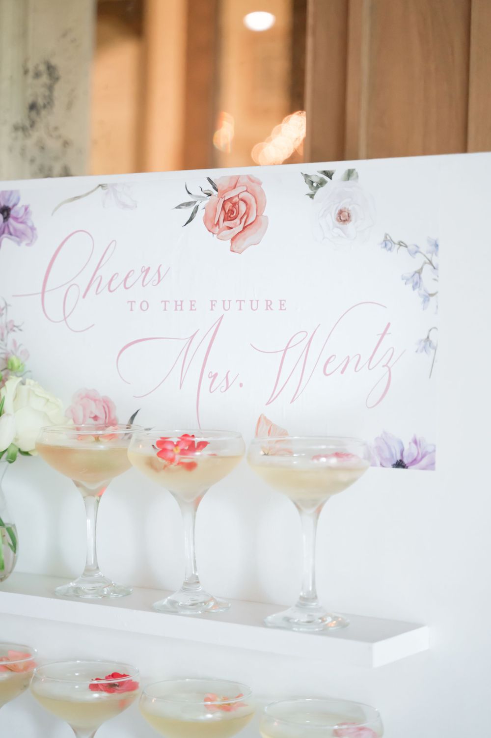 Floral wedding sign with 'Cheers to the future Mrs' text and cocktail glasses.