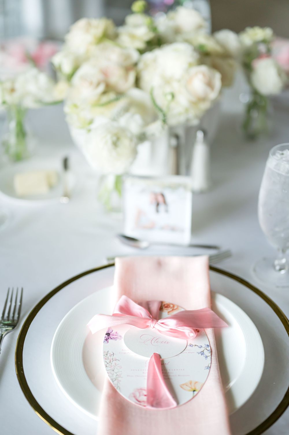 Romantic table setting with white flowers, pink napkin, and decorative place card.