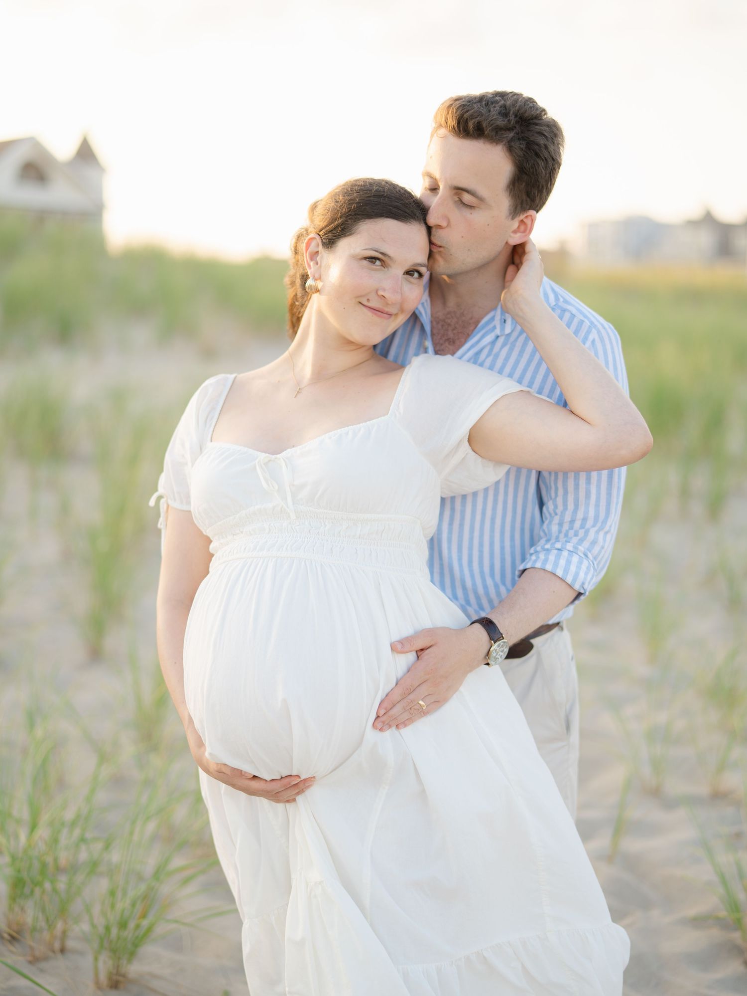 Husband wraps his arms around Mom-to-be posing near historic Victorian cottages near Ocean Grove beach.