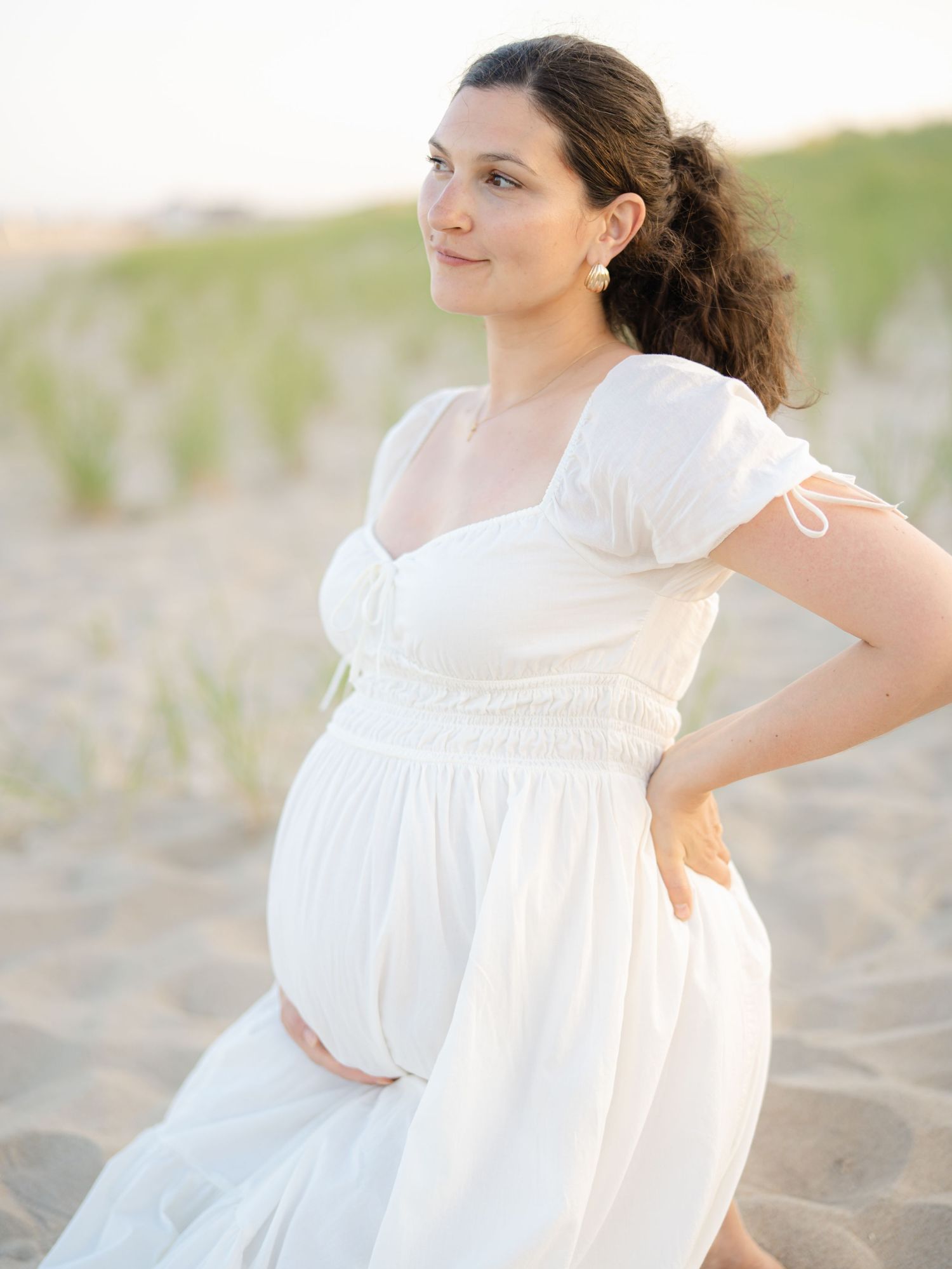 Smiling pregnant woman holding bump on Ocean Grove New Jersey beach.