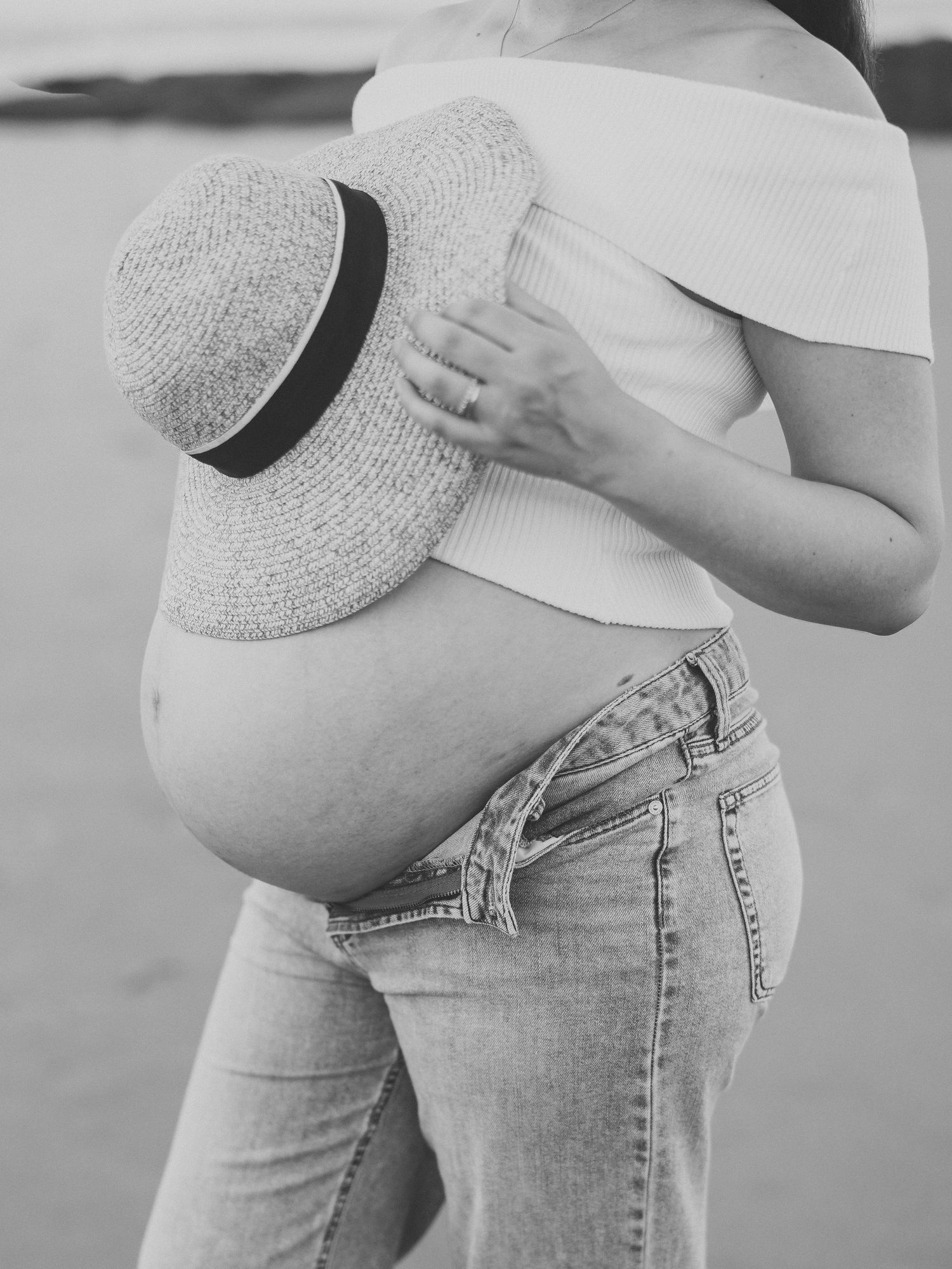 Close up black and white image of pregnant woman with a beach hat over her belly.