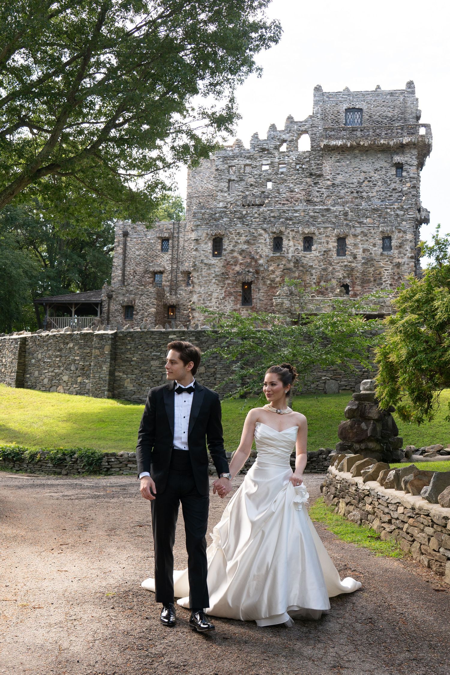 Wedding couple walks hand in hand along a path with a grand stone castle backdrop on their special day.