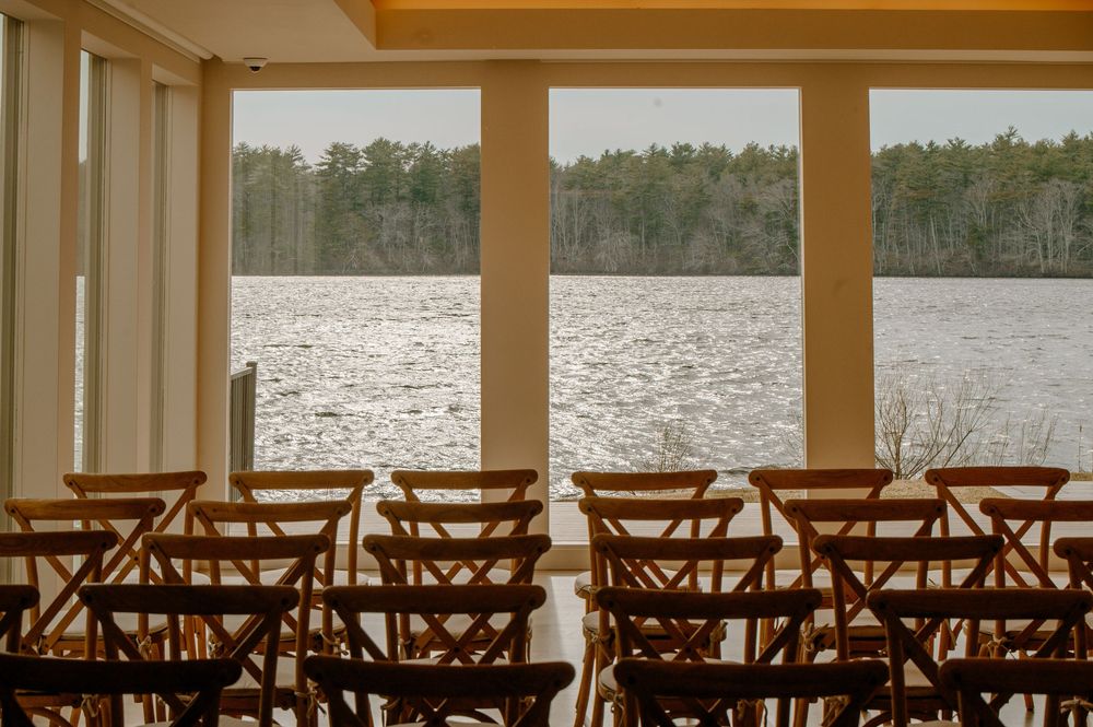 Rows of wooden cross-back chairs set up for a lakeside wedding ceremony with panoramic water views.
