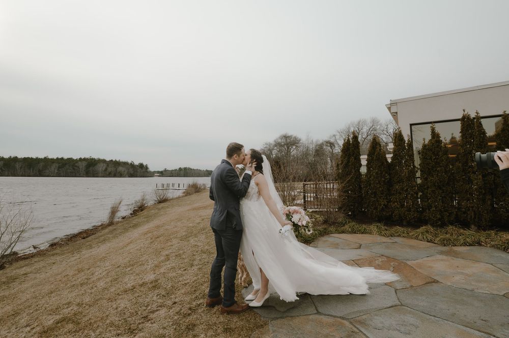 Bride and groom share first kiss on stone patio overlooking serene lake on their wedding day.