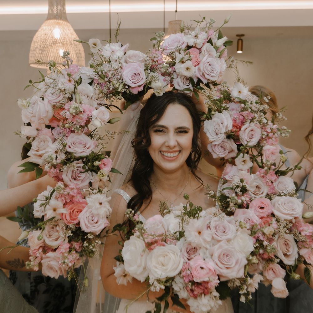 Smiling bride surrounded by lush pink and white rose bouquets on her wedding day.