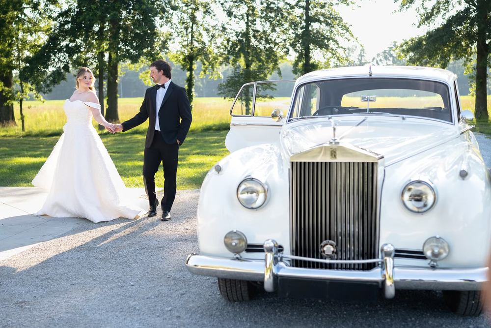 Bride and groom hold hands walking toward a luxury white Rolls-Royce shoe by Sassi Photo