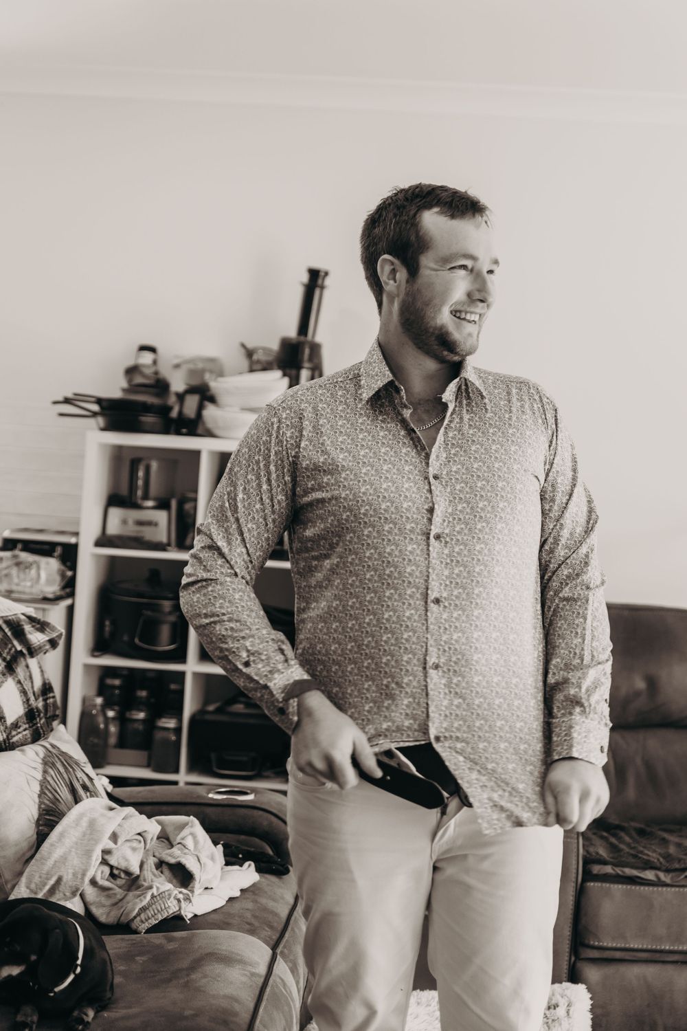 A smiling bearded man in a patterned shirt stands in a room getting ready for a special occasion.