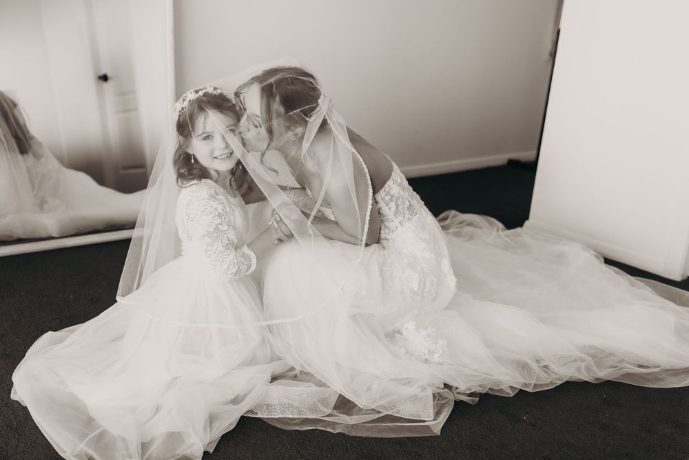 Two brides in white wedding gowns and veils sit together on the floor sharing an intimate moment.
