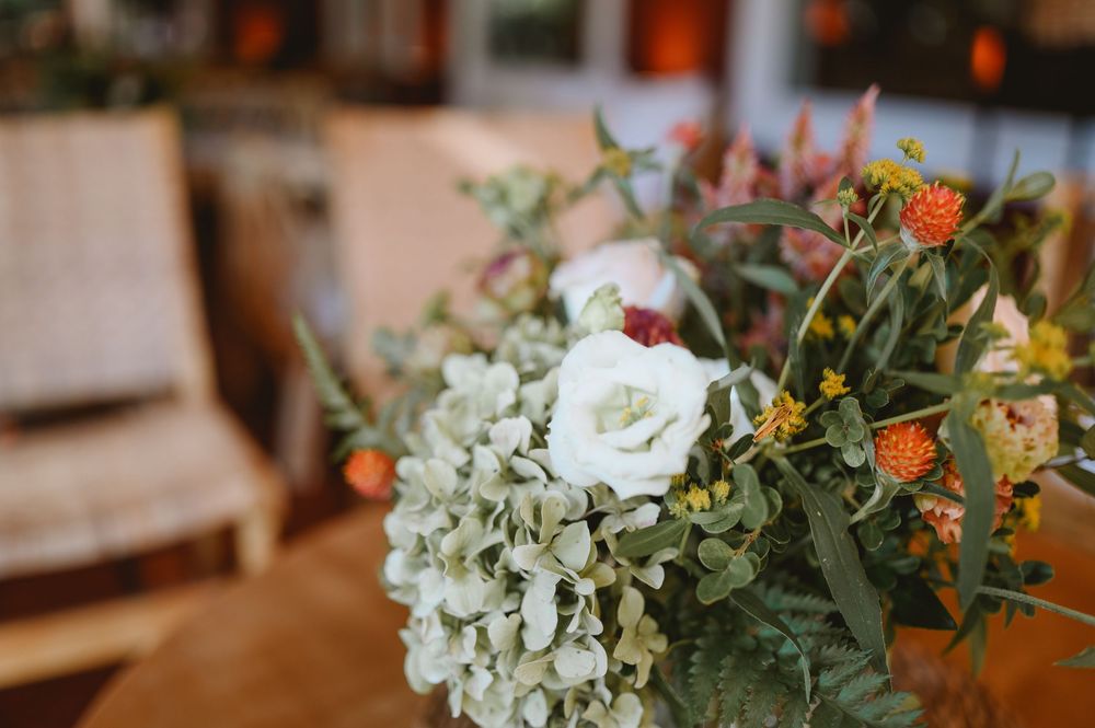 Close-up of a lush wedding bouquet with white roses, hydrangeas, and orange wildflowers with greenery.