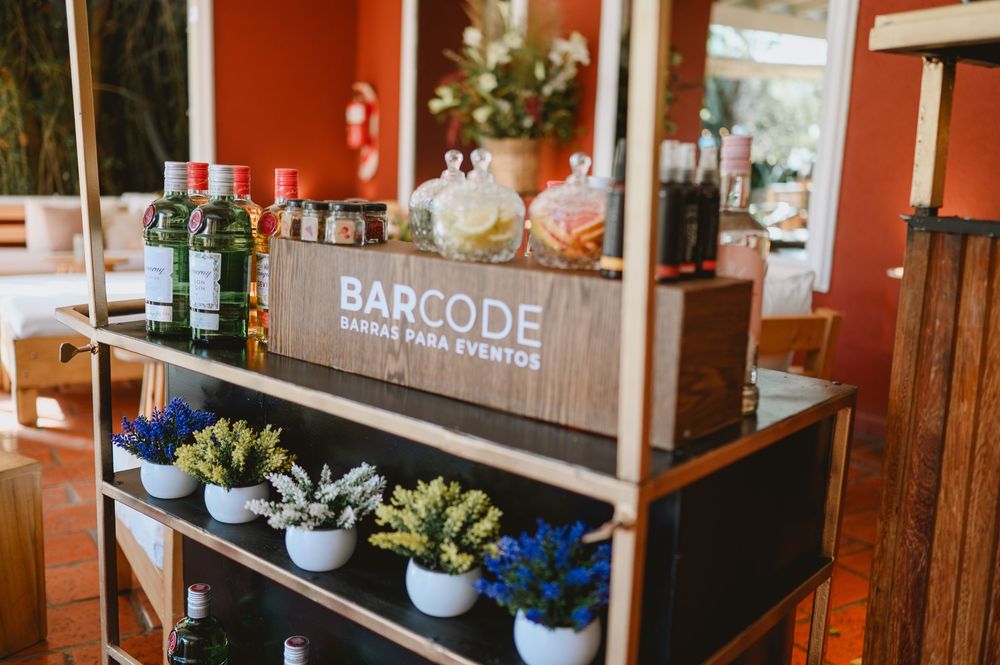 Barcode bar service display shelf with bottles, spices, and small potted plants at an outdoor event.