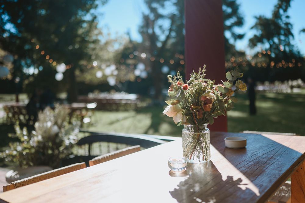 Glass jar with a wildflower bouquet on a wooden table in a sunlit outdoor garden setting.