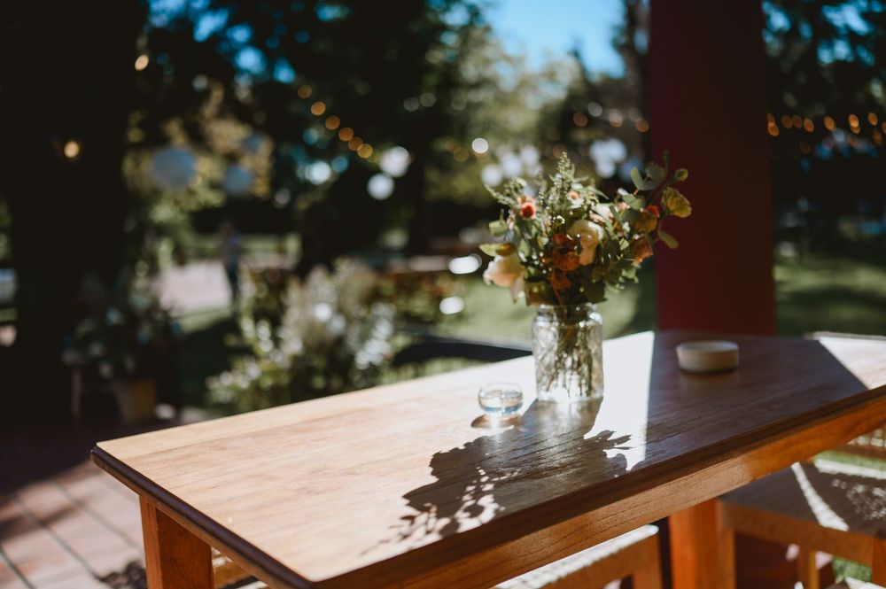 Wildflower bouquet in a glass jar on a wooden table with dappled sunlight in an outdoor garden.