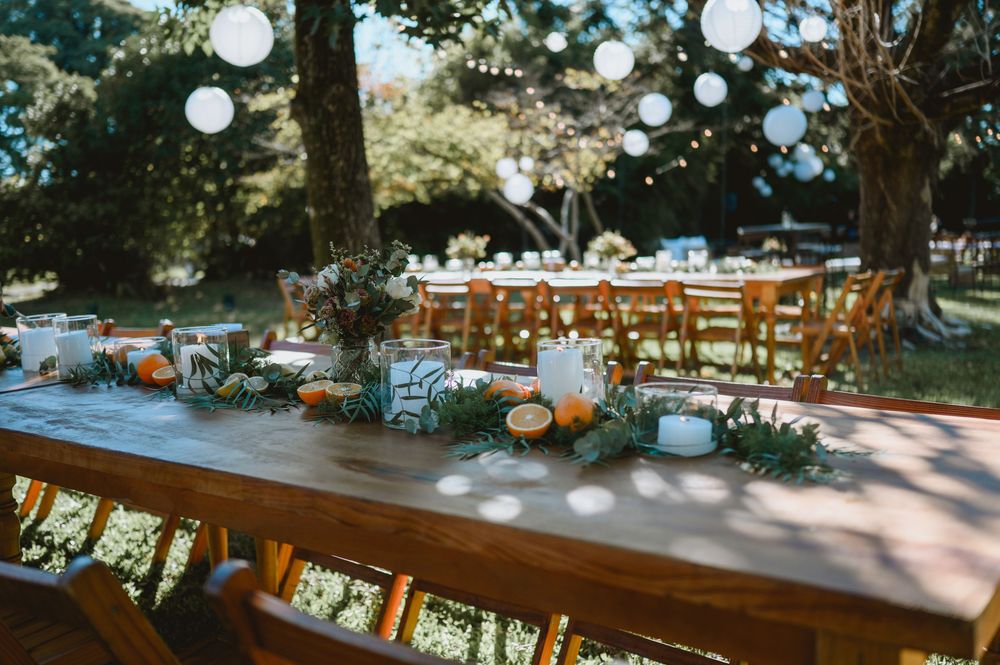 Elegant outdoor wedding reception with long wooden tables, candles, greenery, and globe string lights.