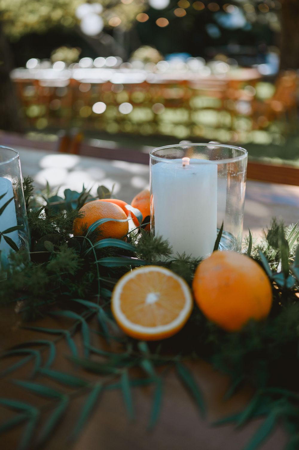Close-up of wedding table decor featuring sliced oranges, candles, and lush green garland centerpiece.